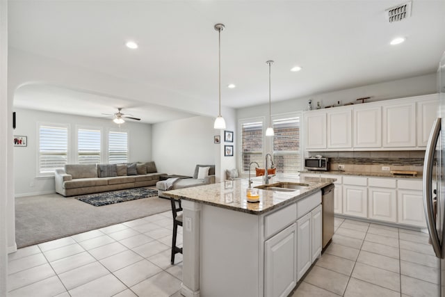 kitchen with light carpet, hanging light fixtures, white cabinetry, a kitchen island with sink, and light stone counters