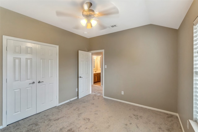 unfurnished bedroom featuring a closet, visible vents, light carpet, vaulted ceiling, and baseboards