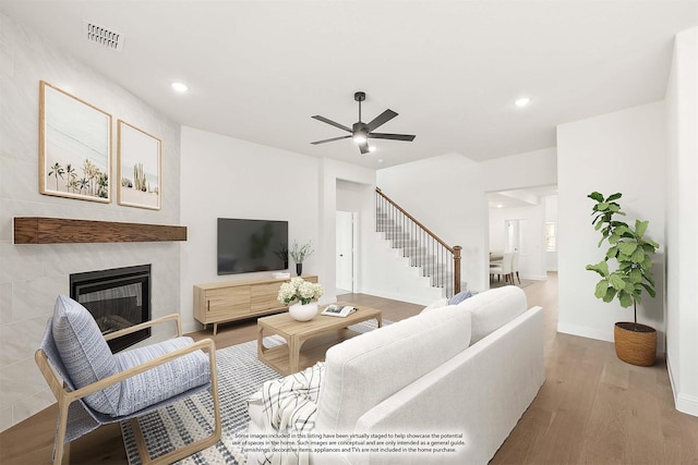 living area featuring ceiling fan, a fireplace, visible vents, stairway, and wood finished floors
