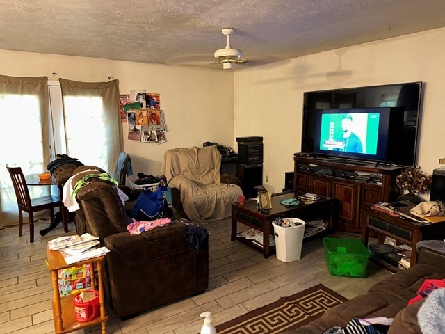 living room featuring a textured ceiling, light wood-type flooring, and ceiling fan