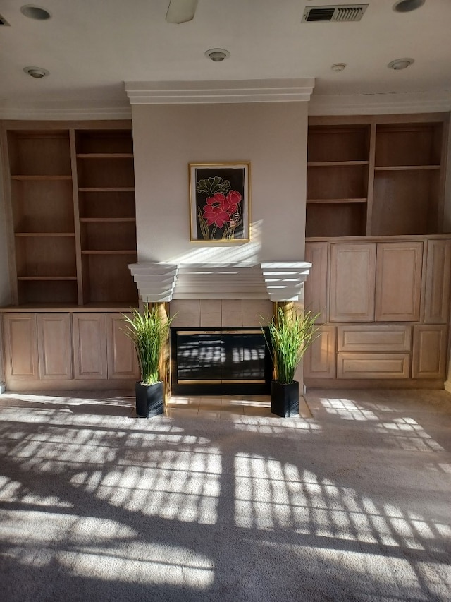 unfurnished room featuring a tiled fireplace, light colored carpet, ornamental molding, and built in features