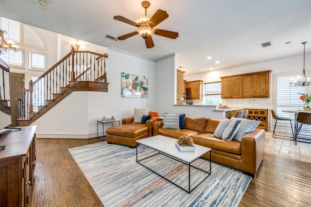 living room featuring wood-type flooring, ornamental molding, and ceiling fan with notable chandelier