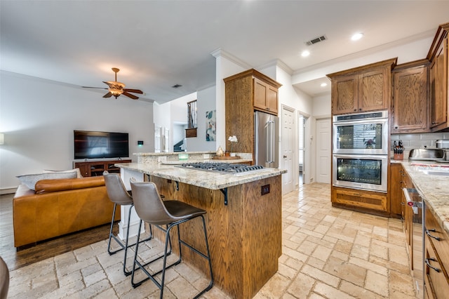 kitchen with decorative backsplash, appliances with stainless steel finishes, a kitchen breakfast bar, light stone countertops, and ornamental molding