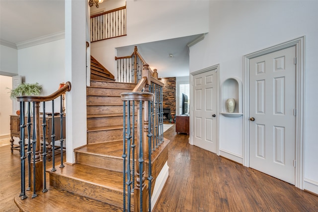 stairs with a stone fireplace, ornamental molding, wood-type flooring, and a high ceiling