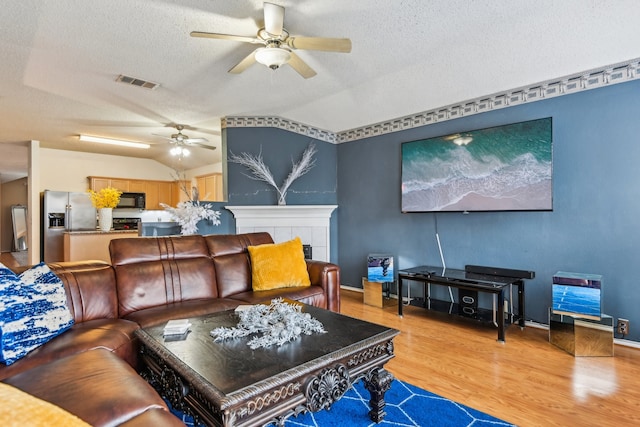 living room featuring a textured ceiling, a tiled fireplace, ceiling fan, lofted ceiling, and light hardwood / wood-style flooring