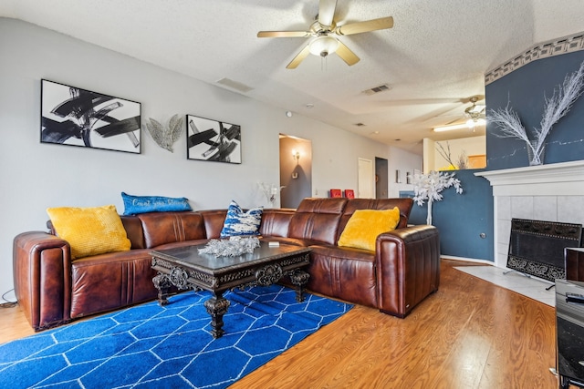 living room featuring a textured ceiling, a fireplace, wood-type flooring, and ceiling fan