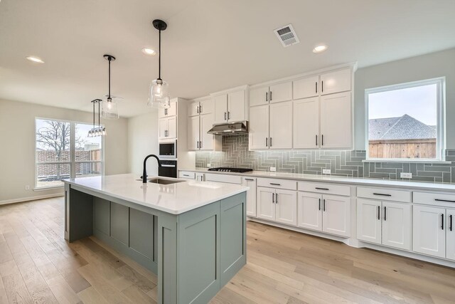 kitchen with white cabinetry, an island with sink, sink, and pendant lighting