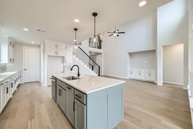 kitchen featuring sink, decorative light fixtures, stainless steel dishwasher, a kitchen island with sink, and white cabinets