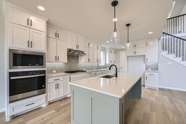 kitchen featuring decorative light fixtures, white cabinetry, an island with sink, sink, and stainless steel appliances