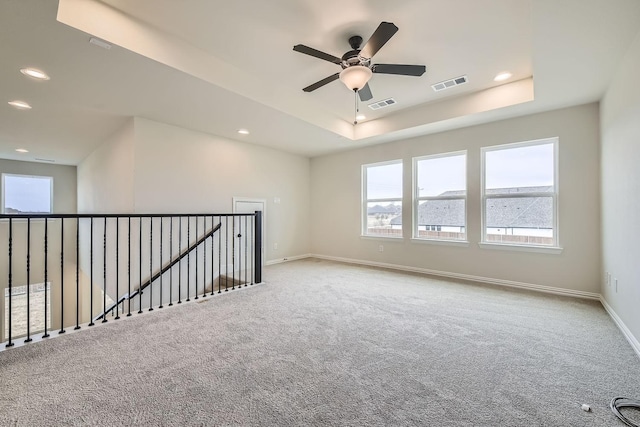 carpeted empty room with ceiling fan and a tray ceiling