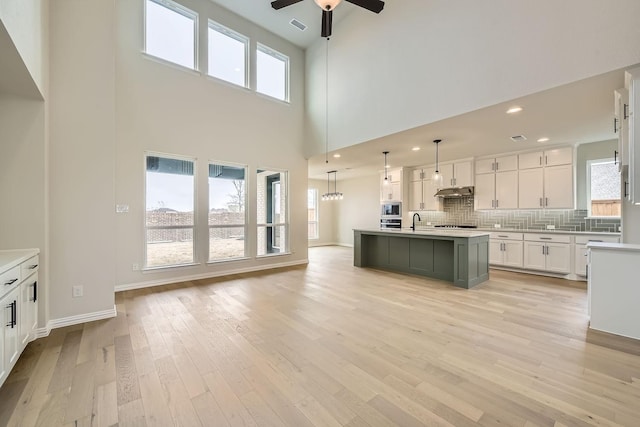 kitchen featuring stainless steel microwave, decorative light fixtures, white cabinetry, an island with sink, and light hardwood / wood-style floors