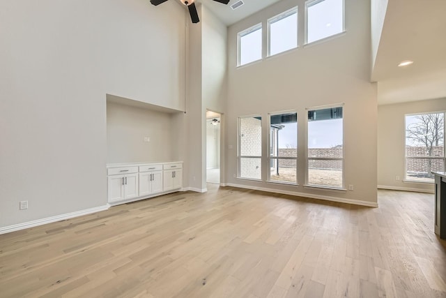 unfurnished living room featuring ceiling fan, light hardwood / wood-style floors, and a towering ceiling