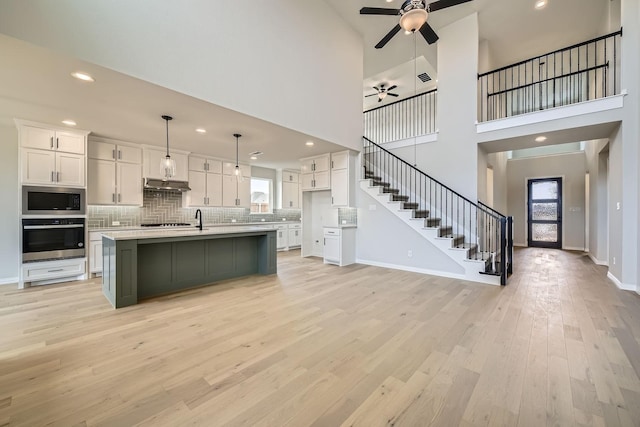 kitchen with white cabinetry, decorative light fixtures, stainless steel appliances, and a center island with sink