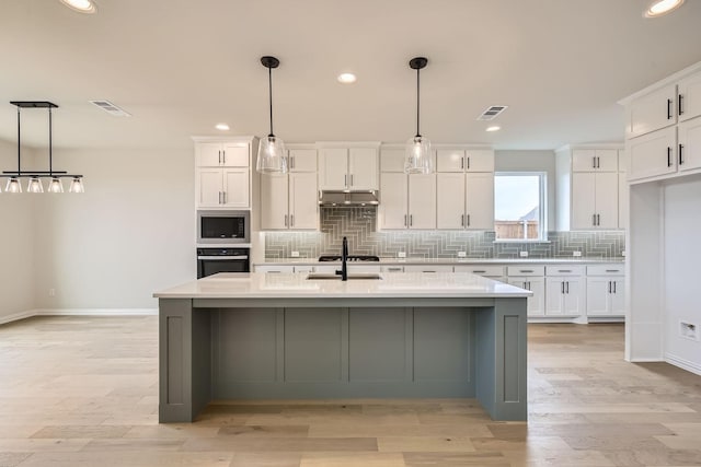 kitchen featuring sink, decorative light fixtures, oven, a kitchen island with sink, and white cabinets