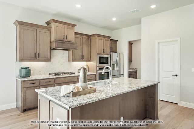 kitchen featuring light stone counters, an island with sink, light hardwood / wood-style flooring, sink, and stainless steel appliances