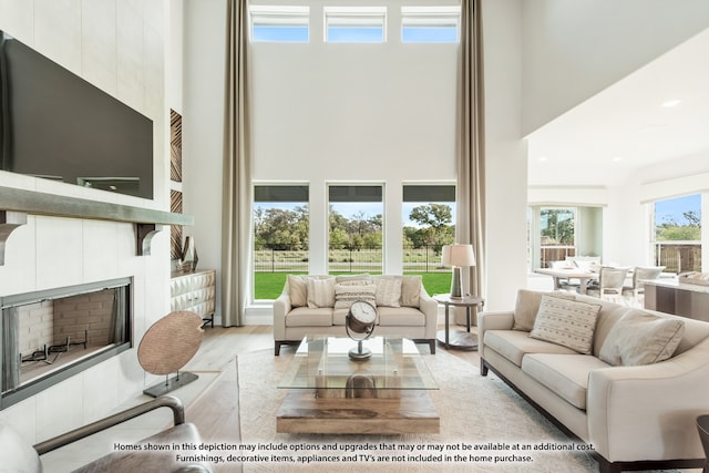 living room featuring a towering ceiling, a tile fireplace, and light wood-type flooring