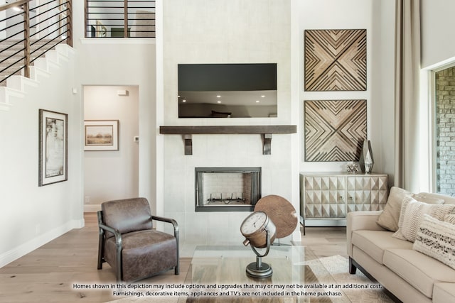 living room with a tile fireplace, wood-type flooring, and a towering ceiling