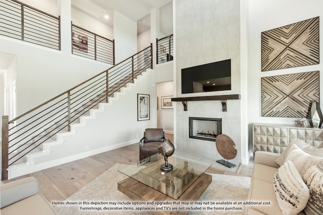 living room featuring a tile fireplace, light hardwood / wood-style floors, and a towering ceiling