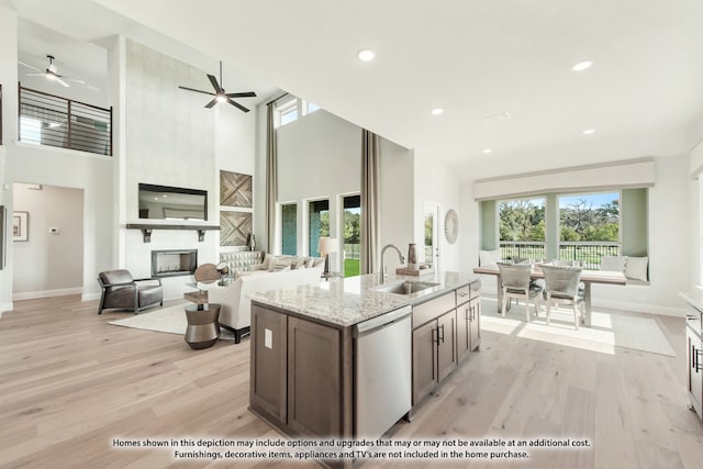 kitchen with stainless steel dishwasher, a high ceiling, a large fireplace, and light hardwood / wood-style floors