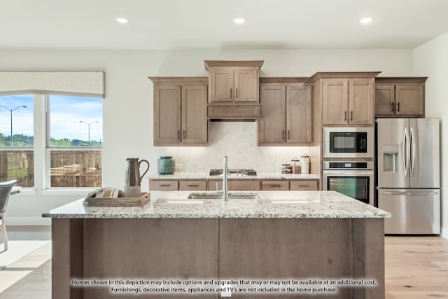 kitchen with decorative backsplash, appliances with stainless steel finishes, sink, light hardwood / wood-style floors, and light stone counters