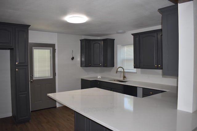 kitchen with kitchen peninsula, a textured ceiling, sink, and dark wood-type flooring