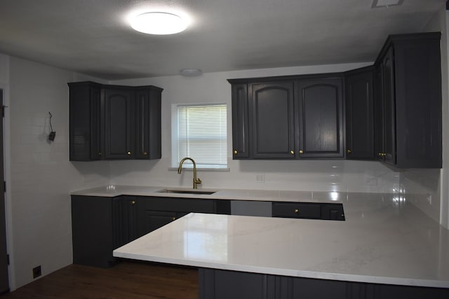 kitchen with dark wood-type flooring, light stone countertops, sink, and kitchen peninsula