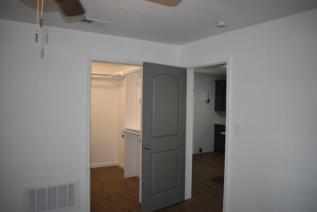 unfurnished bedroom featuring a spacious closet, dark wood-type flooring, a closet, and ceiling fan