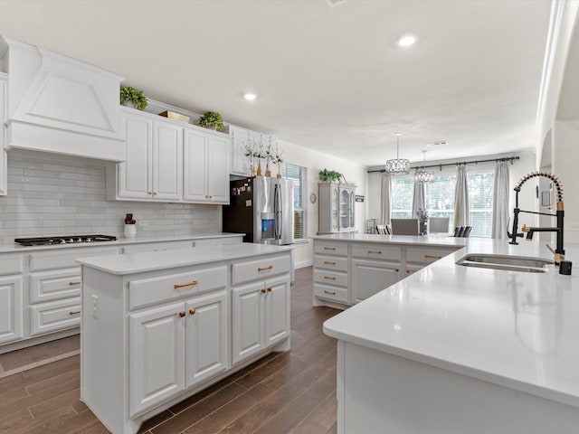 kitchen with sink, a center island, stainless steel fridge with ice dispenser, hanging light fixtures, and white cabinets