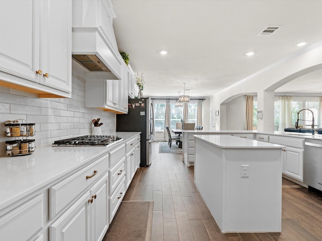 kitchen featuring sink, premium range hood, white cabinetry, appliances with stainless steel finishes, and a kitchen island