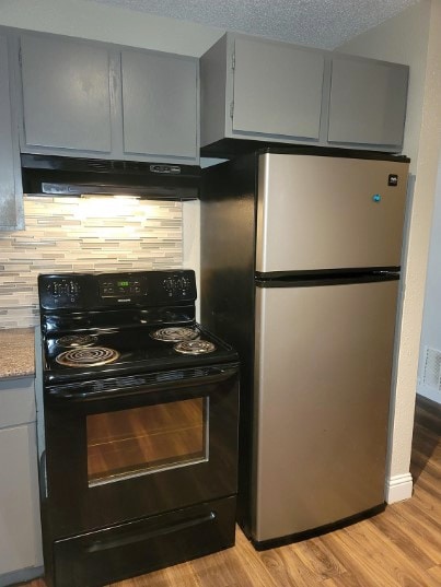 kitchen featuring black electric range, a textured ceiling, decorative backsplash, light hardwood / wood-style floors, and stainless steel refrigerator