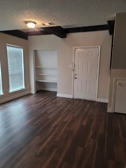 interior space featuring a textured ceiling, lofted ceiling with beams, and dark wood-type flooring