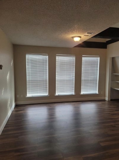 unfurnished room featuring dark wood-type flooring and a textured ceiling