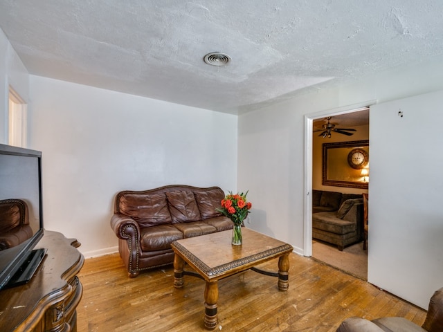 living room with a textured ceiling, light wood-type flooring, and ceiling fan