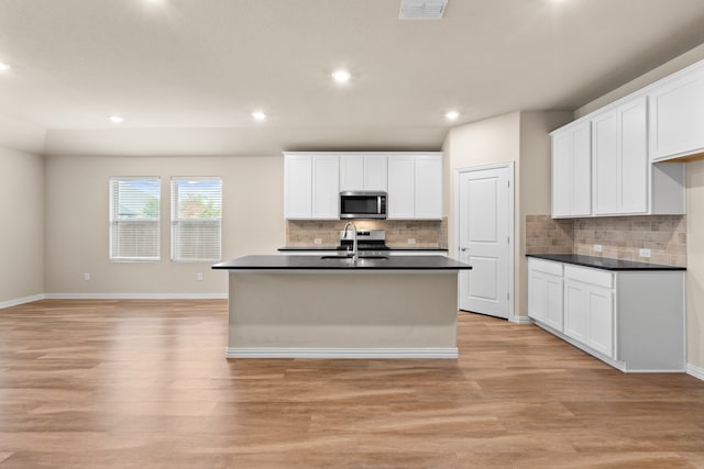 kitchen with white cabinetry, decorative backsplash, light wood-type flooring, and a center island with sink