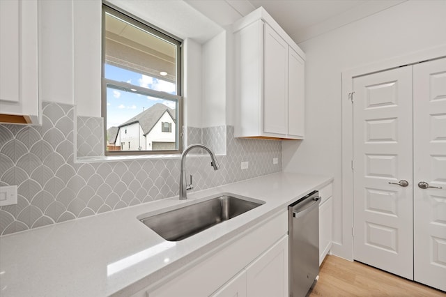 kitchen with decorative backsplash, white cabinetry, stainless steel dishwasher, light hardwood / wood-style flooring, and sink