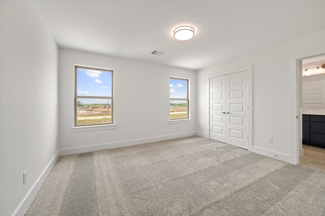 unfurnished bedroom with light carpet, multiple windows, ensuite bath, and a closet