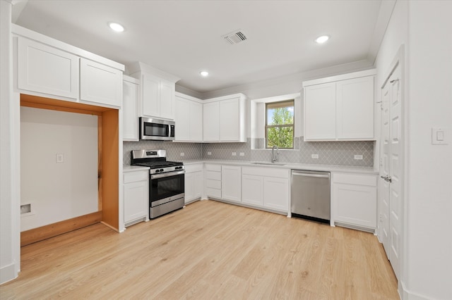 kitchen featuring appliances with stainless steel finishes, sink, light wood-type flooring, white cabinets, and decorative backsplash