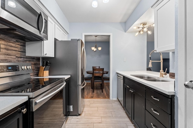 kitchen featuring sink, decorative light fixtures, a notable chandelier, stainless steel appliances, and white cabinets