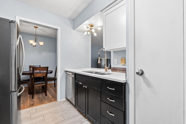 kitchen featuring pendant lighting, sink, white cabinets, a chandelier, and stainless steel appliances