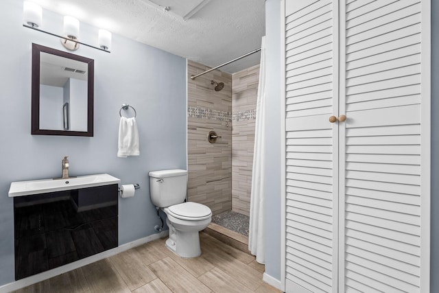 bathroom with vanity, toilet, a textured ceiling, and a tile shower