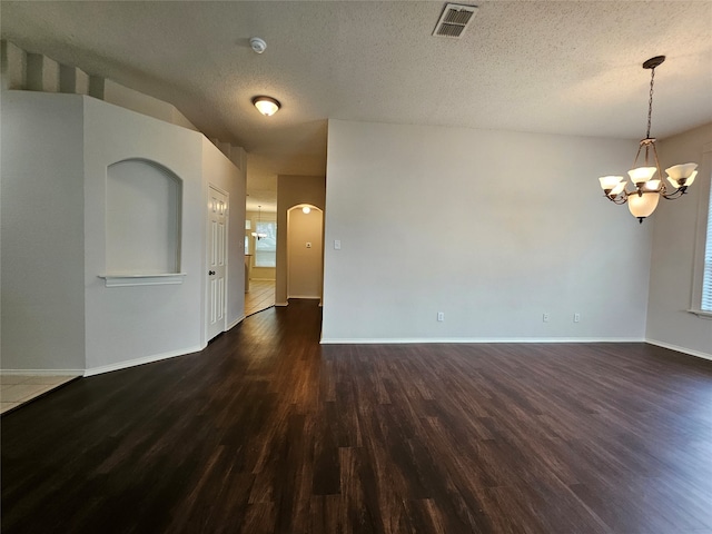 unfurnished room with dark wood-type flooring, a textured ceiling, and a notable chandelier