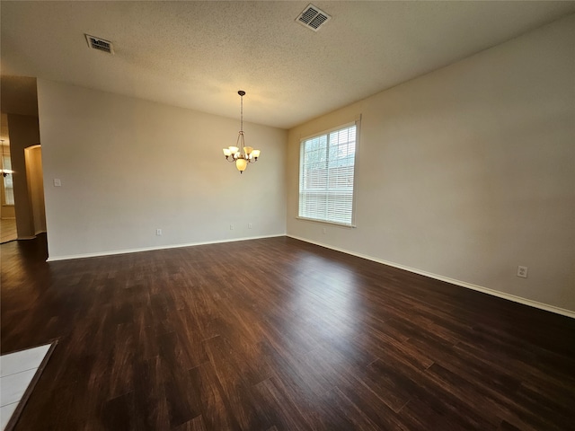 empty room featuring a textured ceiling, dark hardwood / wood-style floors, and a chandelier