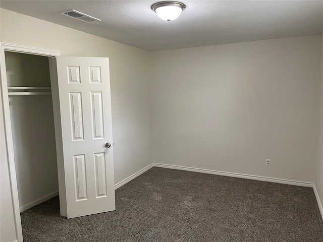 unfurnished bedroom featuring a textured ceiling, dark carpet, and a closet