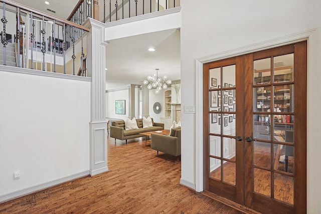 hallway featuring french doors, a high ceiling, ornate columns, hardwood / wood-style flooring, and a chandelier