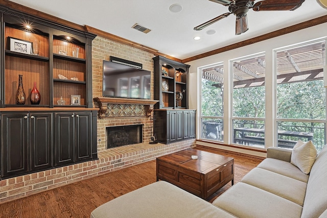 living room with ornamental molding, a healthy amount of sunlight, hardwood / wood-style flooring, and a brick fireplace