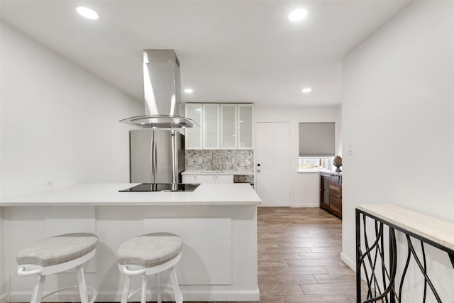 kitchen with island range hood, hardwood / wood-style floors, white cabinetry, and stainless steel refrigerator