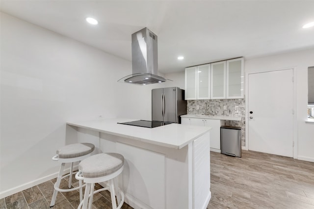 kitchen with kitchen peninsula, island exhaust hood, white cabinets, stainless steel refrigerator, and light hardwood / wood-style flooring