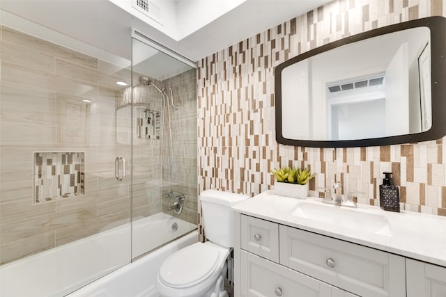 full bathroom with tasteful backsplash, shower / bath combination with glass door, toilet, tile walls, and vanity