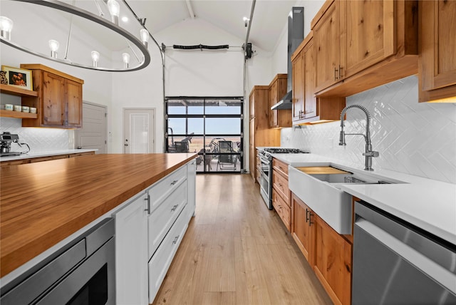 kitchen with high vaulted ceiling, butcher block counters, sink, stainless steel appliances, and light wood-type flooring