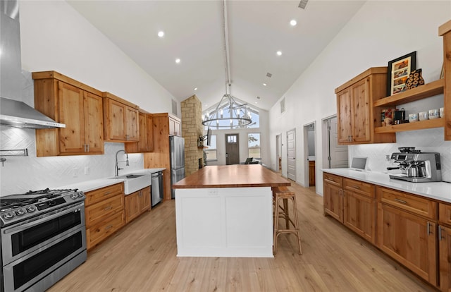 kitchen with stainless steel appliances, light hardwood / wood-style floors, an inviting chandelier, a center island, and wall chimney range hood